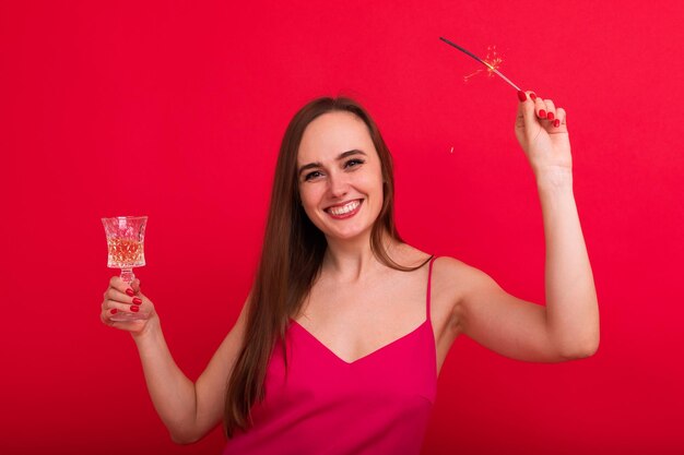 Ambiance festive vacances de Noël Une jeune femme avec du champagne et des cierges pose sur un fond rouge dans le studio