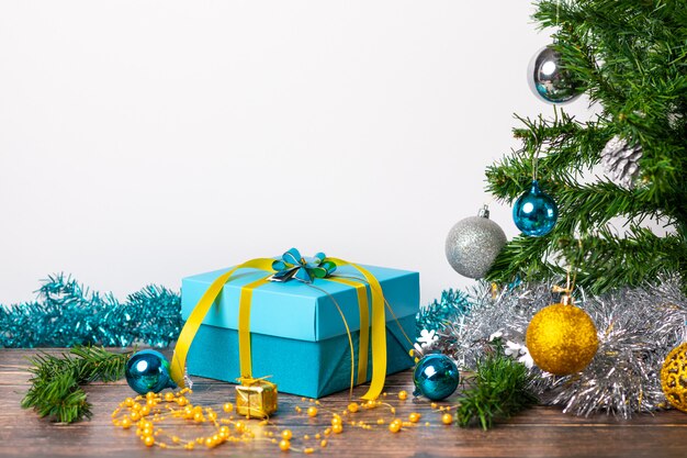 Ambiance de Noël. Un cadeau avec des boules bleues emballées dans un emballage et de petits cadeaux en or situés sur une table en bois et sur un fond blanc. La magie.