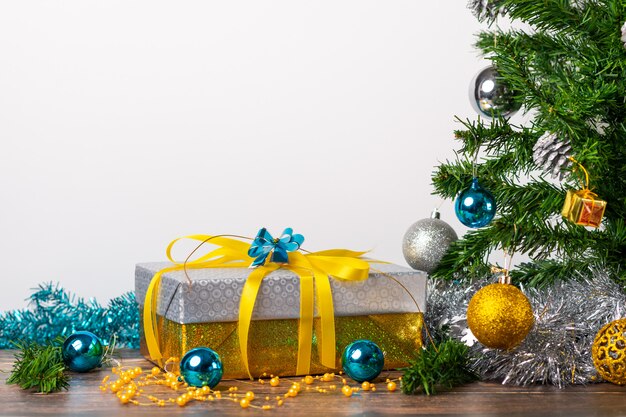 Ambiance de Noël. Un cadeau avec des boules bleues emballées avec des emballages en or et en argent et de petits cadeaux en or situés sur une table en bois et sur un fond blanc. Nouvel An.