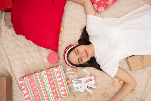 Ambiance de Noël Une jeune fille est allongée sur le lit à la maison parmi les cadeaux du nouvel an, les yeux fermés en souriant