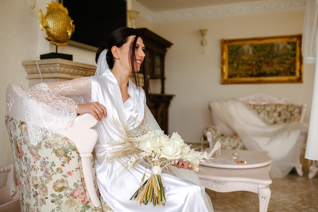 Ambiance romantique du matin de la mariée Mariée dans une maison Préparation du matin de la mariée Mariée en belle robe près du mannequin avec robe à l'intérieur à la maison