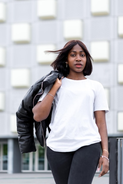 Ambiance urbaine à la mode Une jeune femme noire prend la pose dans un t-shirt blanc élégant et un pantalon noir avec un bâtiment gris comme toile de fond urbaine chic