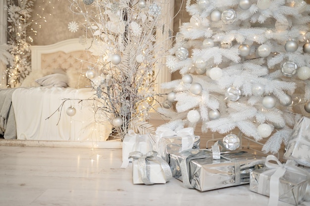 Photo ambiance de vacances du nouvel an intérieur minimaliste élégant du nouvel an cadeaux et cadeaux emballés sous le sapin de noël grande chambre blanche avec lit blanc