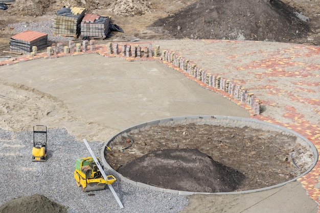 Amélioration des dalles de la cour, travaux inachevés de pose des dalles. Pose de nouvelles dalles de pavage saupoudrées de sable et de tas de tuiles figurées prêtes à être posées