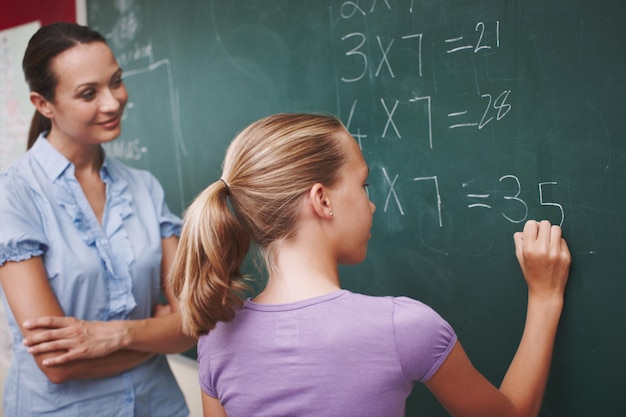 Photo améliorer ses mathématiques une jolie jeune enseignante aidant son élève à résoudre un problème de mathématiques au tableau noir