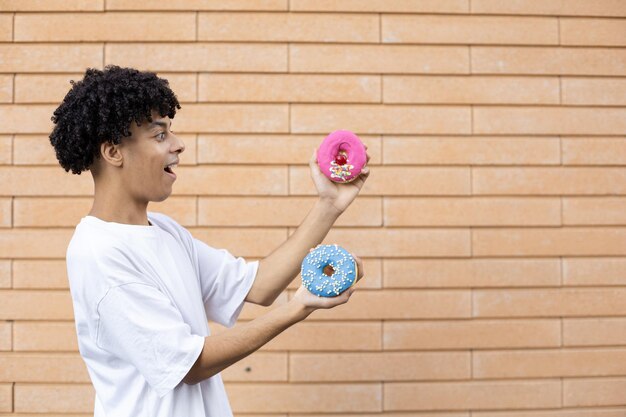 Un Américain debout sur le côté portant un t-shirt blanc tenant un beignet rose et bleu sur le côté