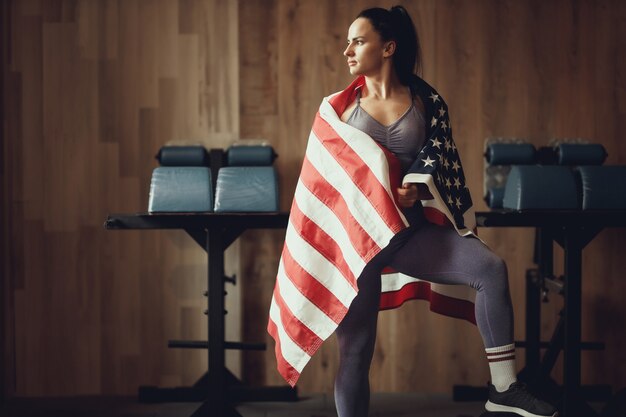 American patriot girl avec un physique athlétique posant sur un fond de mur en bois recouvert d'un drapeau USA