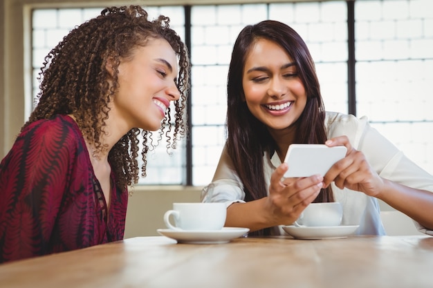 Amies ayant un café et en regardant un smartphone