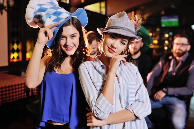 amies en chapeaux bavarois souriant au fond du bar lors de la célébration de la fête de la bière