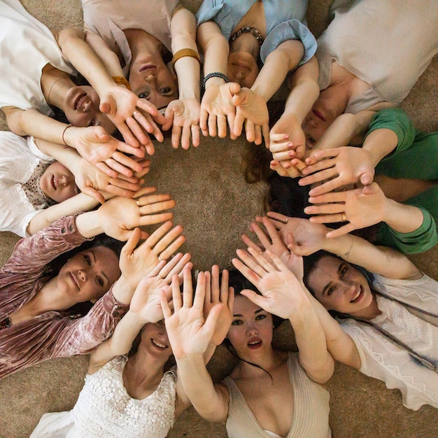 Photo amies heureux couché cercle levant les mains ensemble appréciant la collaboration d'amitié