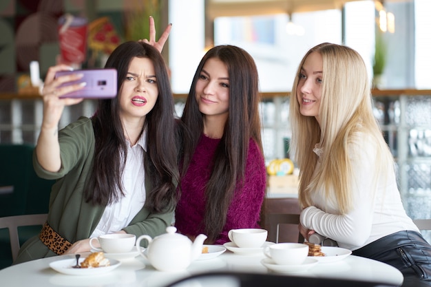 Les amies s'amusent au café en buvant du thé et en se faisant des selfies