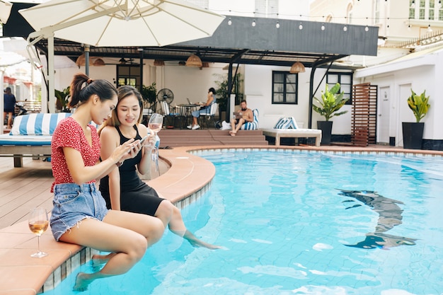 Amies avec smartphone assis à la piscine