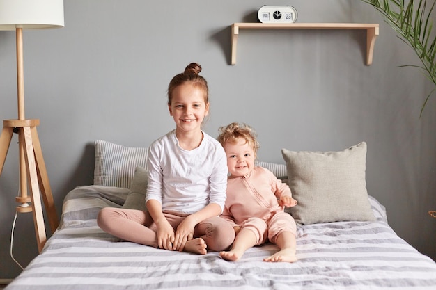 Des amies ou des sœurs à la maison se détendent ensemble en jouant sur le lit dans la chambre en regardant la caméra portant des vêtements décontractés s'amusant le matin le week-end