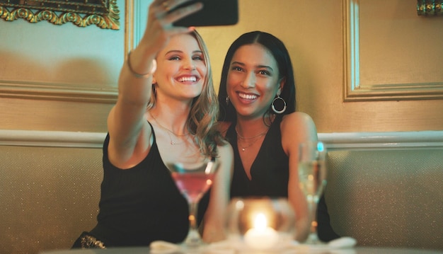 Des amies téléphonent et selfies dans une boîte de nuit pour un cocktail avec des femmes heureuses et de l'alcool Sourire photo mobile et boissons au restaurant de personnes lors d'un événement pour le nouvel an ou l'happy hour