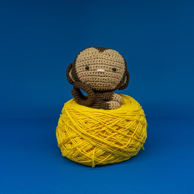 Amigurumi de singe assis sur une pelote de laine jaune. fond bleu