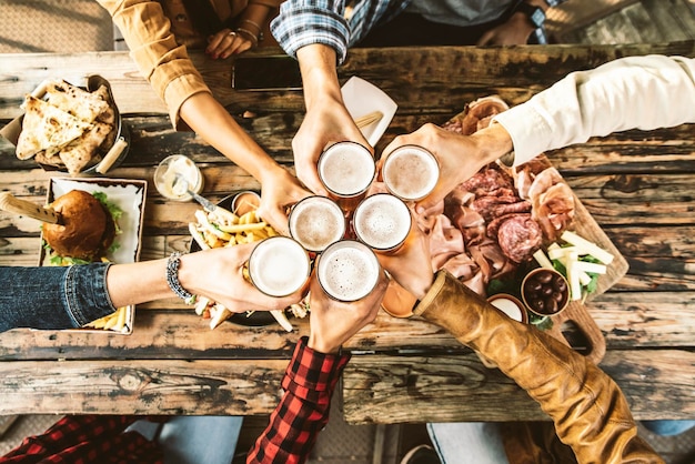 Amis acclamant des verres à bière sur une table en bois recouverte de plats délicieux