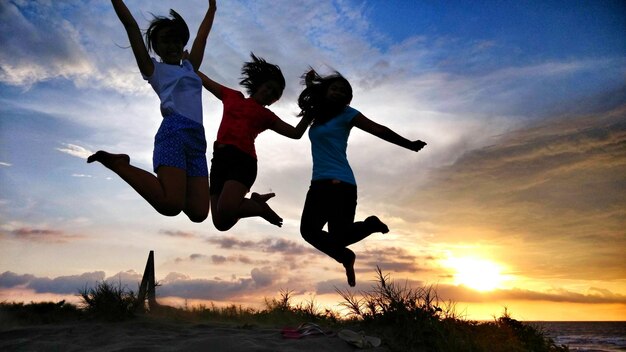 Photo des amis adolescents sautent sur la plage au coucher du soleil.