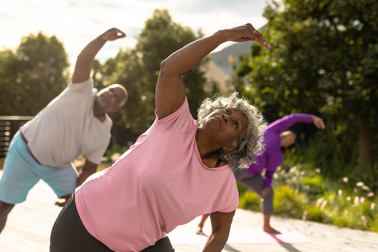 Photo des amis âgés multiraciaux pratiquant le yoga contre des plantes dans le jardin pendant l'été