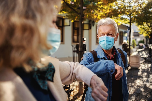 Amis aînés avec des masques debout à l'extérieur et saluent avec leurs coudes.