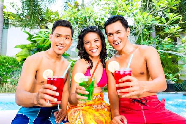 Amis asiatiques buvant des cocktails au bord de la piscine