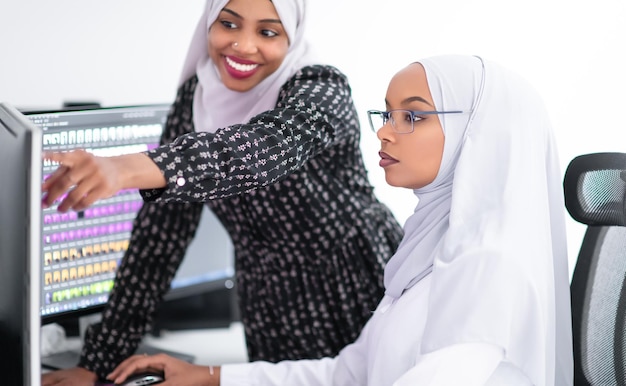 Photo amis au bureau deux jeunes femmes d'affaires musulmanes modernes afro-américaines portant un foulard sur un lieu de travail de bureau créatif et lumineux avec grand écran