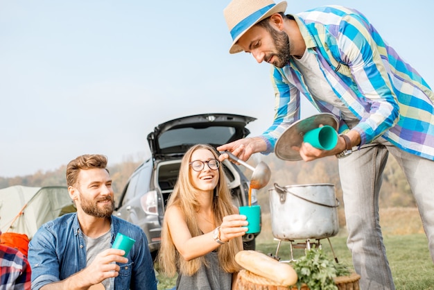 Amis ayant un délicieux dîner avec une soupe cuite au chaudron pendant le pique-nique au camping