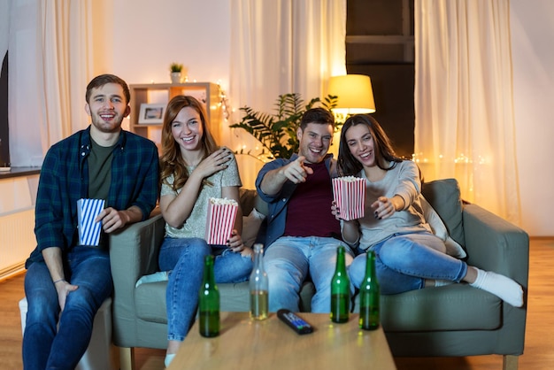 Des amis avec de la bière et du pop-corn en train de regarder la télévision à la maison.