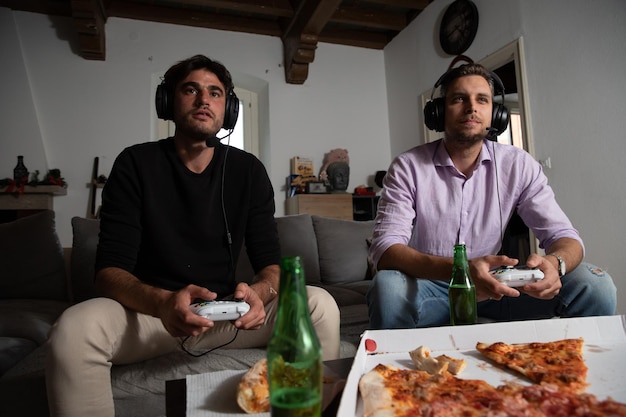 Amis concentrés jouant dur et vite aux jeux vidéo avec de la pizza et de la bière sur la table