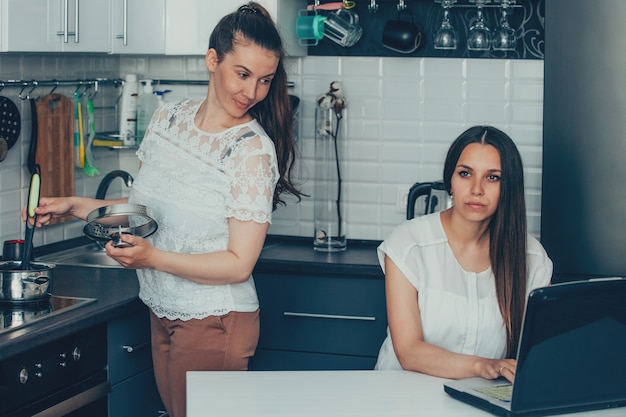 Amis dans la cuisine travaillant sur un ordinateur portable et cuisine