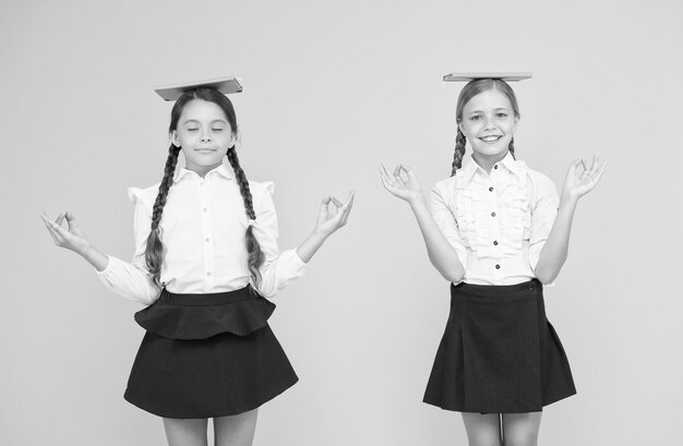 Amis d'écolières étudiant ensemble L'uniforme scolaire des enfants tient des livres Équilibre de vie Faire face au stress scolaire Pratiquer la méditation Trouver l'équilibre Concept d'harmonie Paix et équilibre Espoir pour le mieux