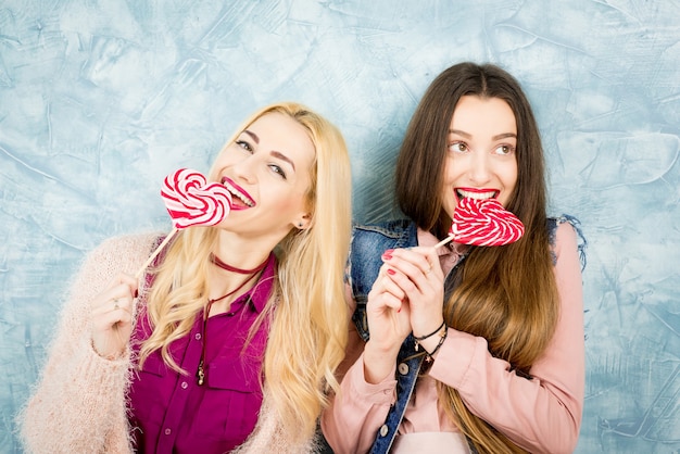 Photo amis élégants féminins s'amusant avec des bonbons sur le fond bleu du mur