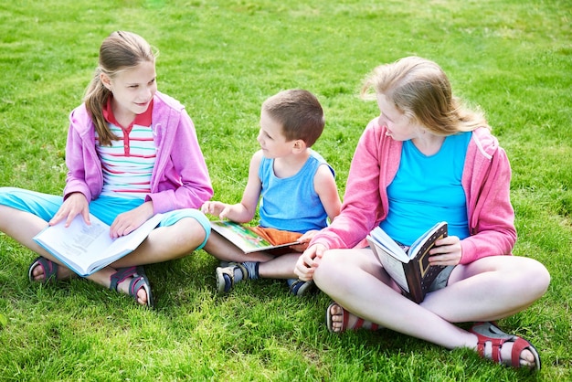 Amis enfants lisant un livre en plein air sur l'herbe