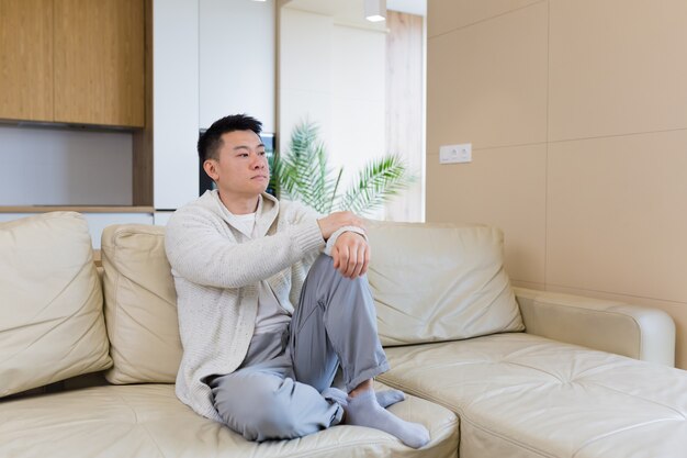Amis ennuyés jeune homme asiatique assis sur un canapé à la maison seul