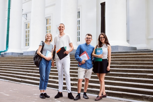 Des amis étudiants masculins et féminins souriants se tiennent en plein air près de l'entrée de l'université