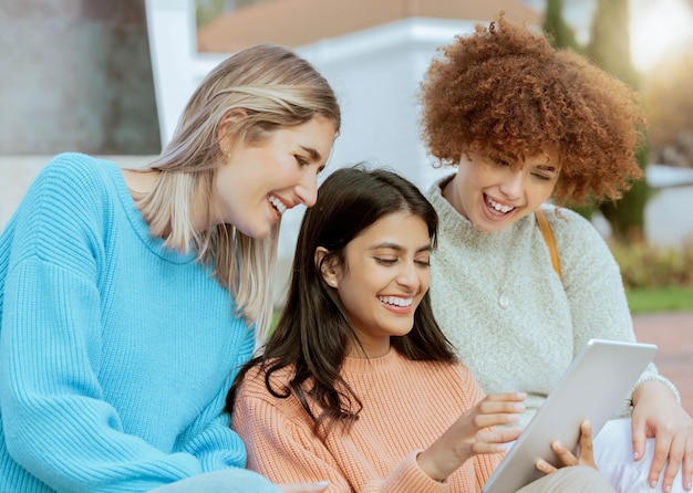 Des amis étudiants et une tablette rient pour les médias sociaux meme ou le divertissement en ligne en streaming sur le campus Des femmes heureuses partagent le rire pour une blague amusante, discutent ou publient sur un écran tactile ensemble à l'université