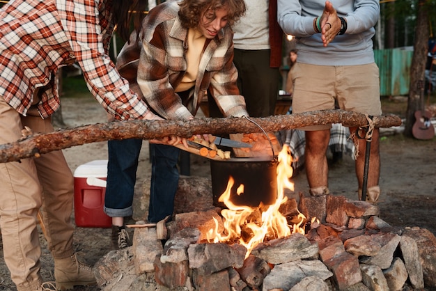 Amis faisant cuire la nourriture ensemble sur un feu pendant le pique-nique dans la forêt