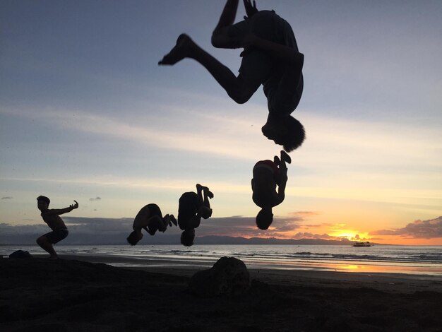 Photo des amis faisant un saut en saut sur la plage contre le ciel au coucher du soleil