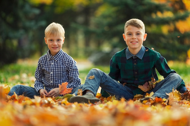 Photo les amis des garçons s'assoient dans le parc sur le sol dans des feuilles d'automne orange vif. beauté de la nature.