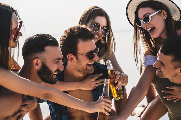 Les amis heureux avec des bouteilles profitent de l'été à la plage