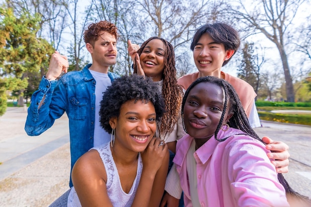 Des amis heureux et diversifiés prenant un selfie de groupe dans un parc.