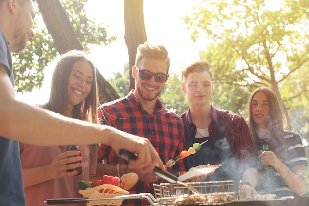 Amis heureux grillant de la viande et profitant d'une soirée barbecue à l'extérieur.