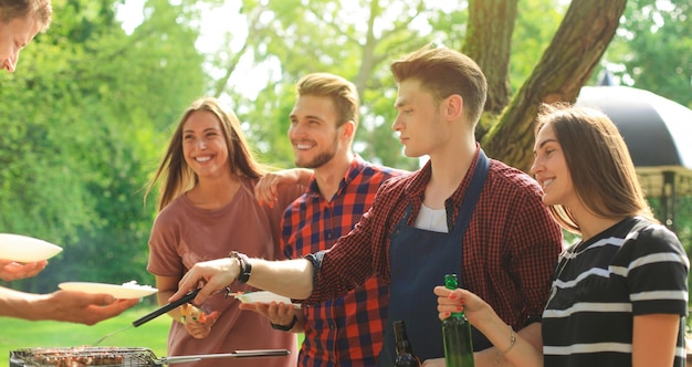 Amis heureux grillant de la viande et profitant d'une soirée barbecue en plein air