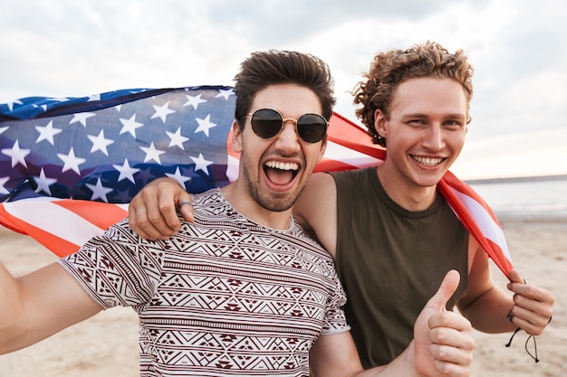 Amis heureux passant du temps à la plage, tenant le drapeau américain