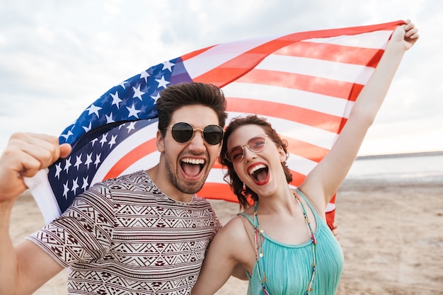 Amis heureux passant du temps à la plage, tenant le drapeau américain