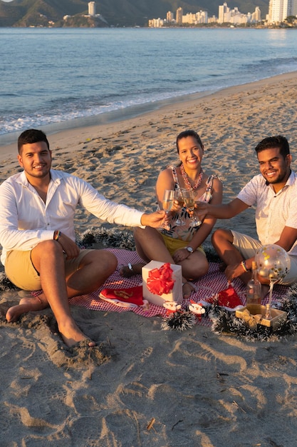 Des amis heureux souriant et proposant un toast alors qu'ils s'assoient pour célébrer le Nouvel An sur la plage.