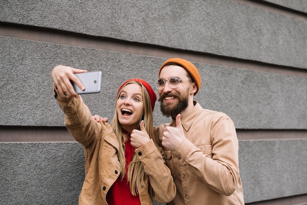 Amis hipster positifs et souriants prenant des selfies ensemble, montrant le coup