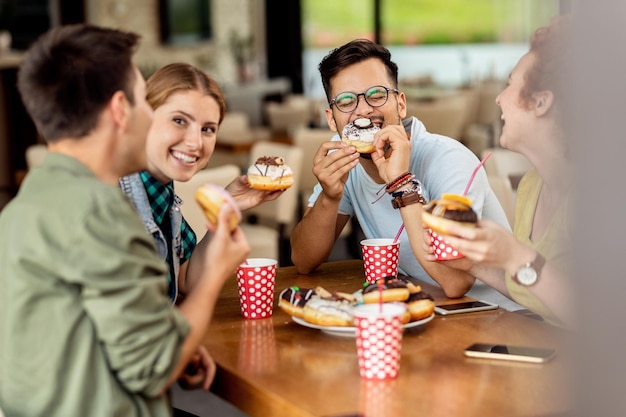 Amis insouciants s'amusant en mangeant des beignets et en parlant dans un café