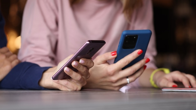 Amis de jeunes femmes sont assis à table avec des téléphones mobiles en gros plan mains