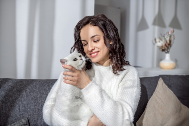 Amis. Jolie jeune femme assise sur le canapé et étreignant son chat