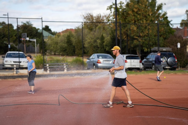 des amis jouant au tennis sur un terrain d'argile arrosant et emballant un terrain dargile faisant l'entretien d'un terrain de tennis